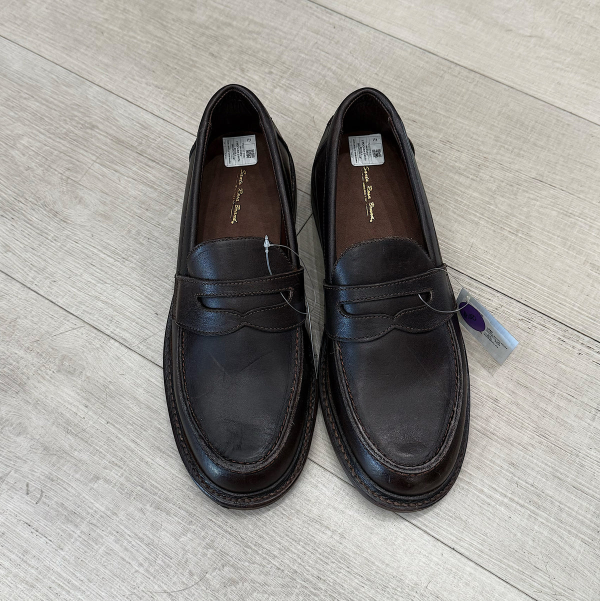 Pair of dark brown leather loafers on a light wooden floor.