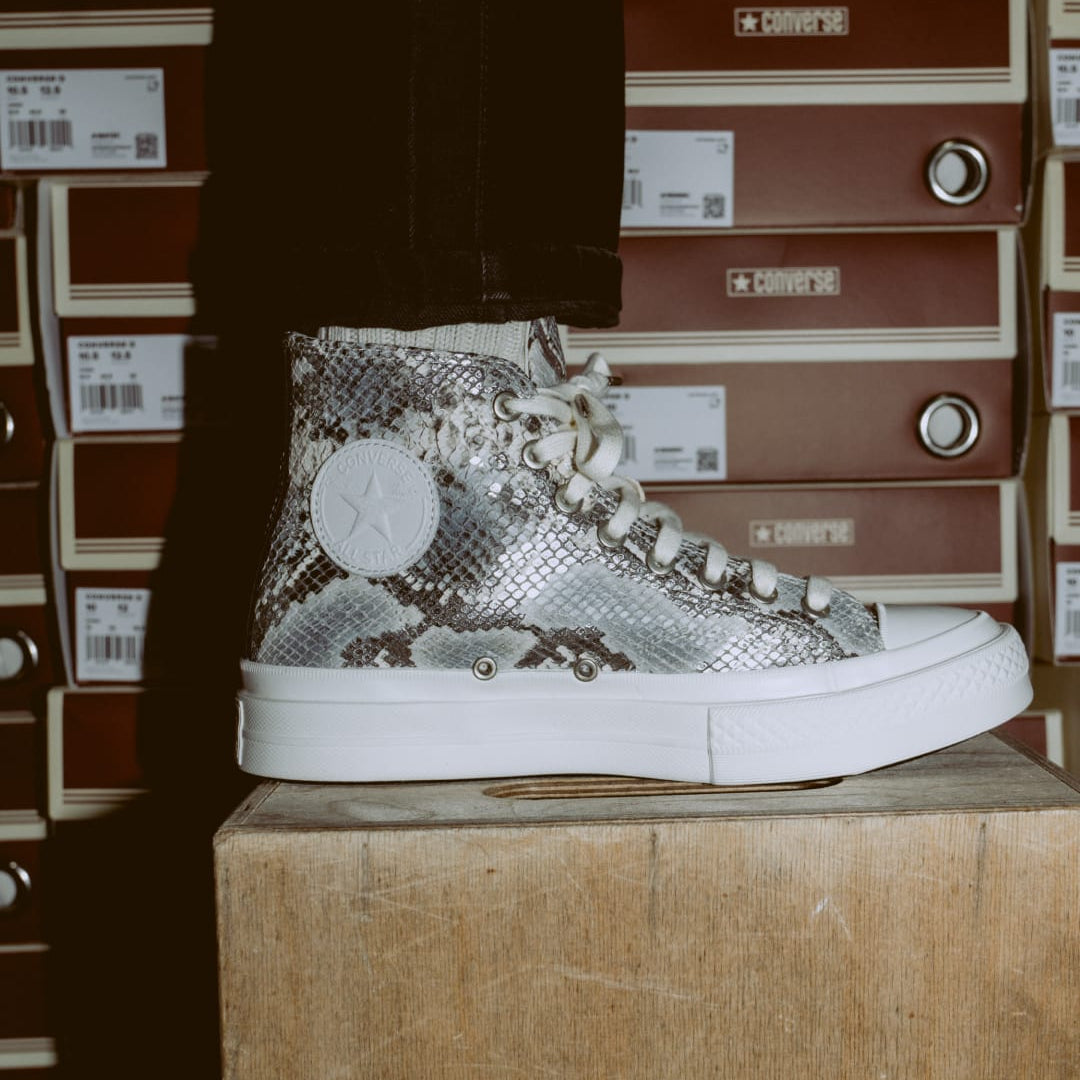 High-top sneaker with snake print and white sole on a wooden box against storage boxes background