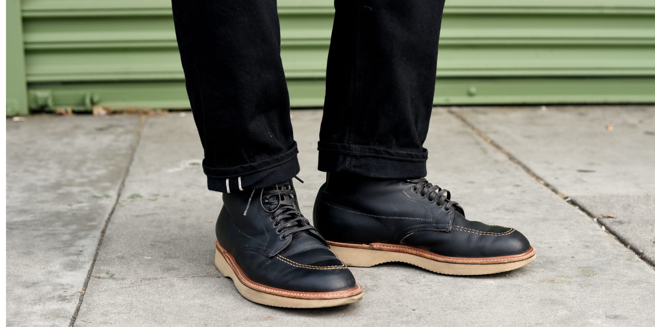 Black leather shoes with brown soles worn by a person on a sidewalk.
