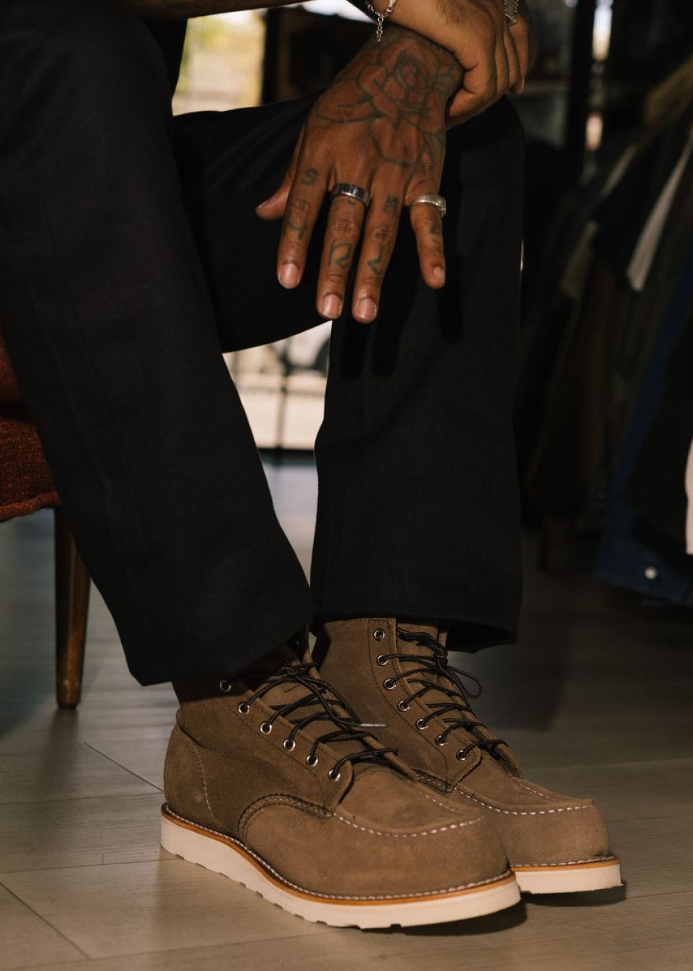 A person wearing brown suede lace-up work boots with black pants, sitting in a store or room setting.