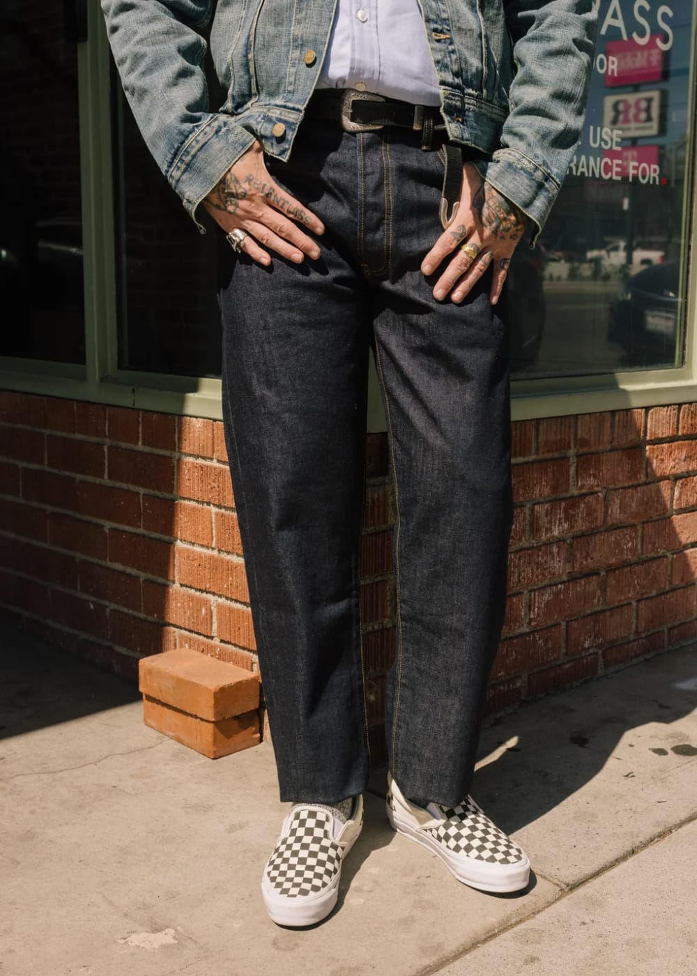 person wearing dark washed denim jeans, paired with a denim jacket and slip-on shoes