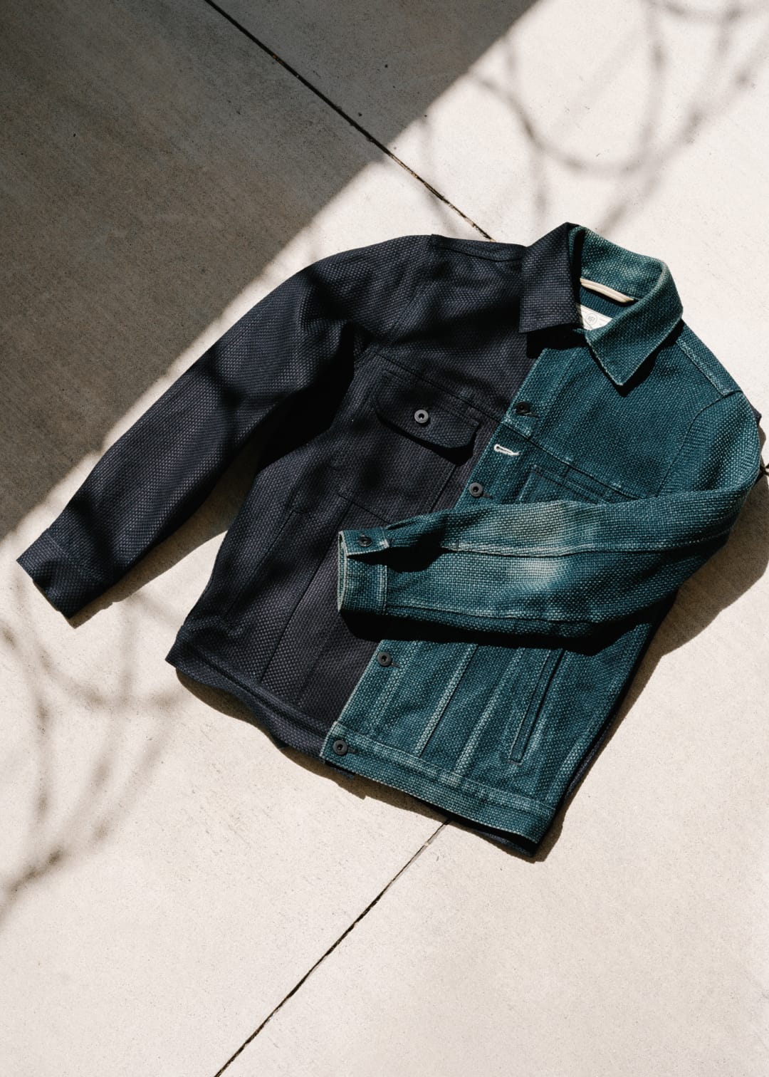 Two denim jackets, one black and one blue, on a light surface with shadows.