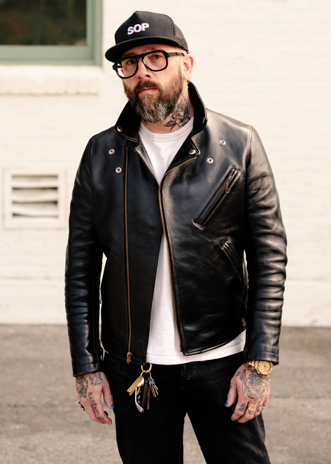 Man wearing a black leather jacket, white t-shirt, and black cap with text.