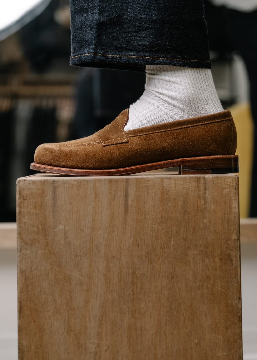 Brown loafers worn with white socks on a wooden block, blurred background