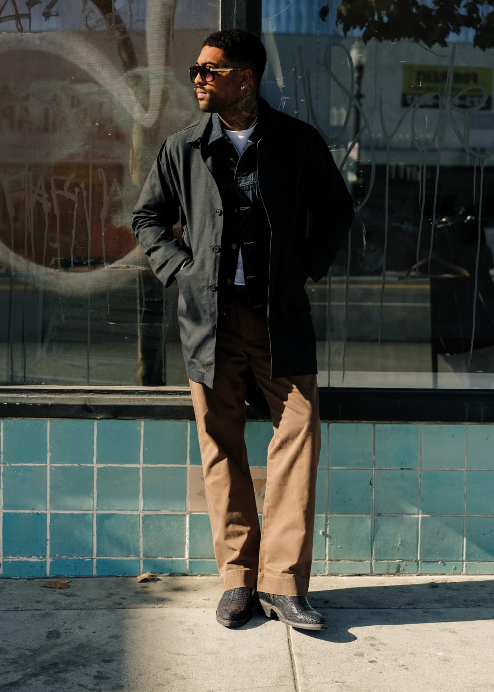 Man standing in front of a wall with graffiti, wearing sunglasses and casual clothing.