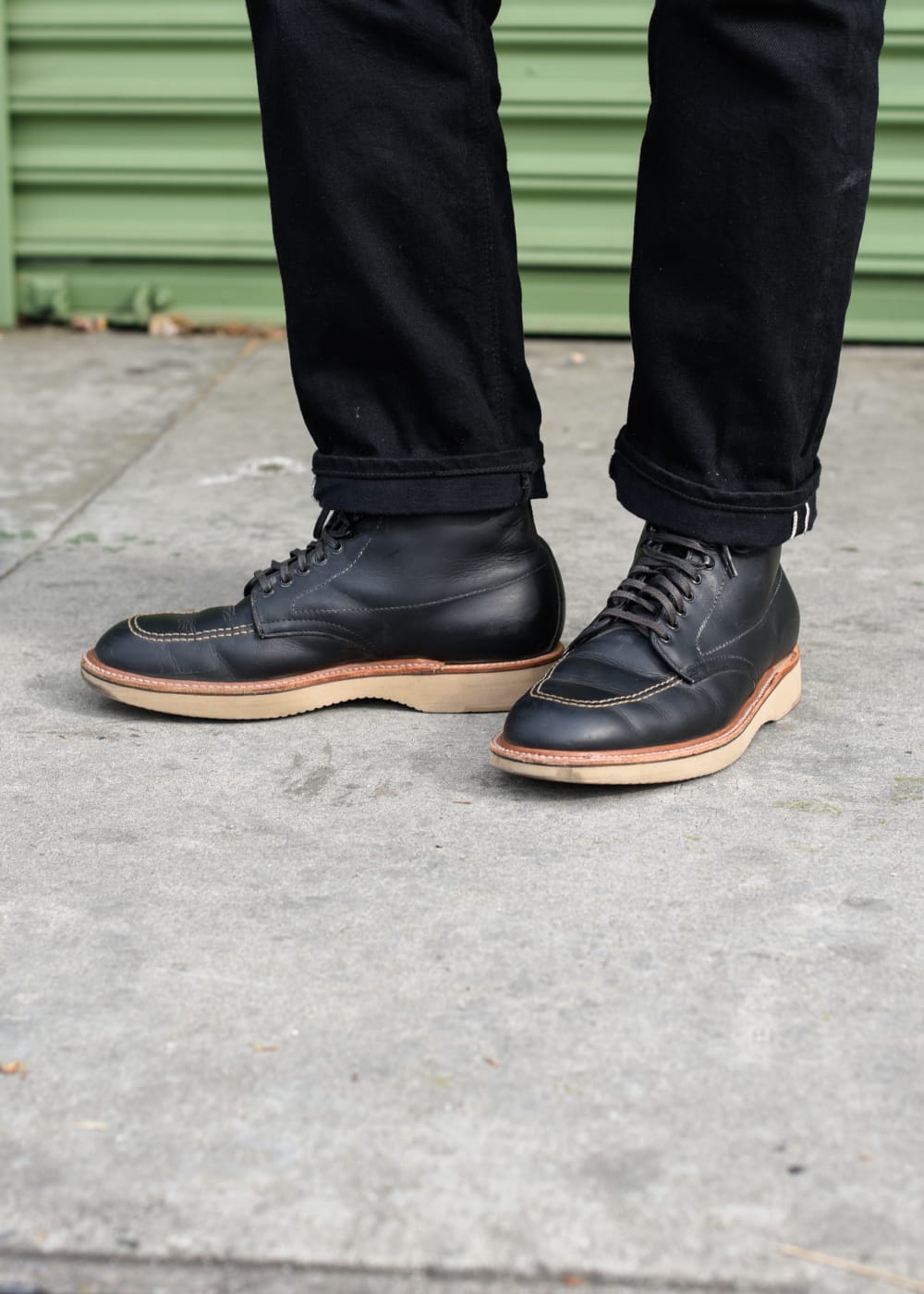 Black leather shoes with brown soles worn by a person on a sidewalk.