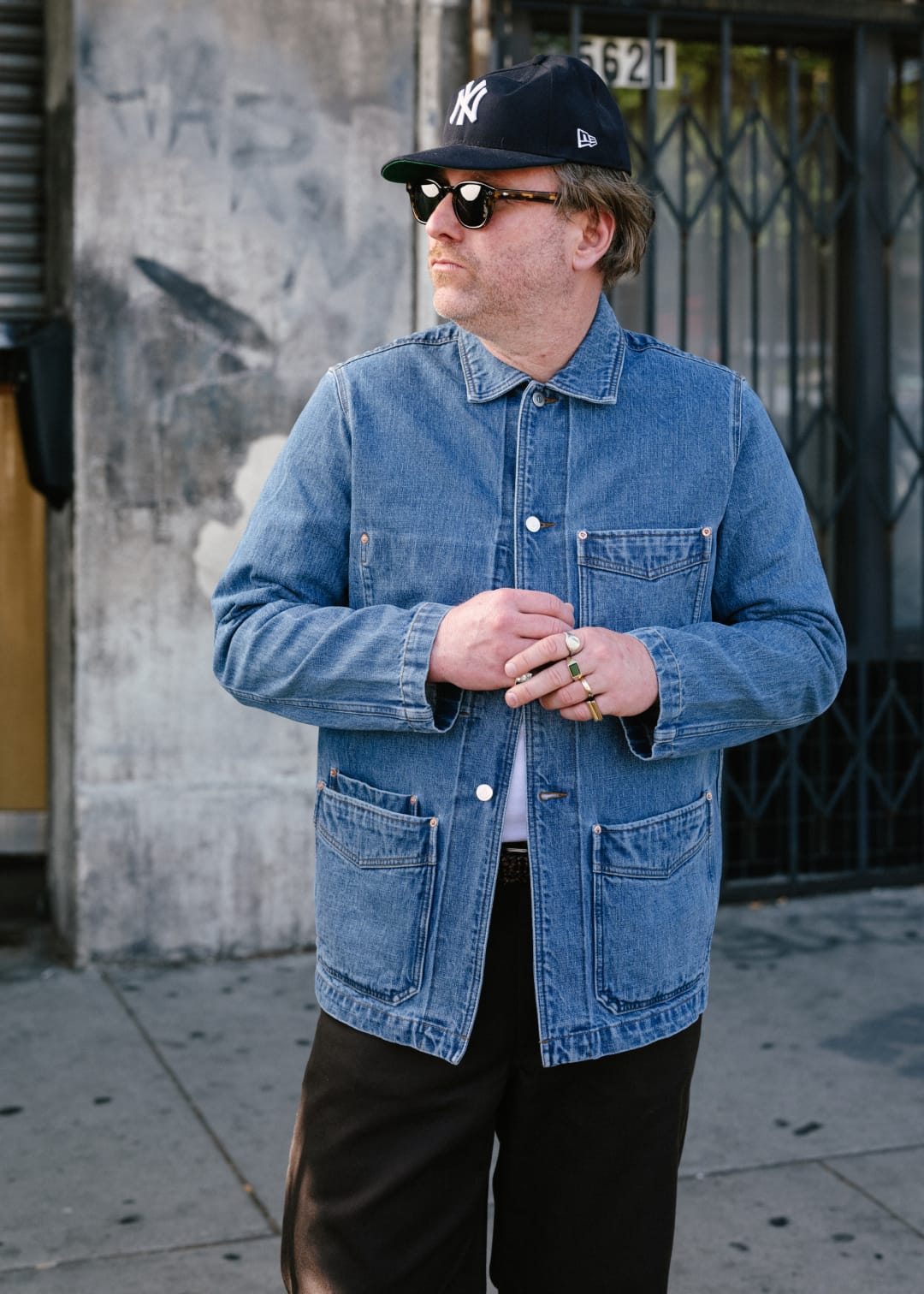 Man wearing a blue denim jacket and black cap standing on a street.