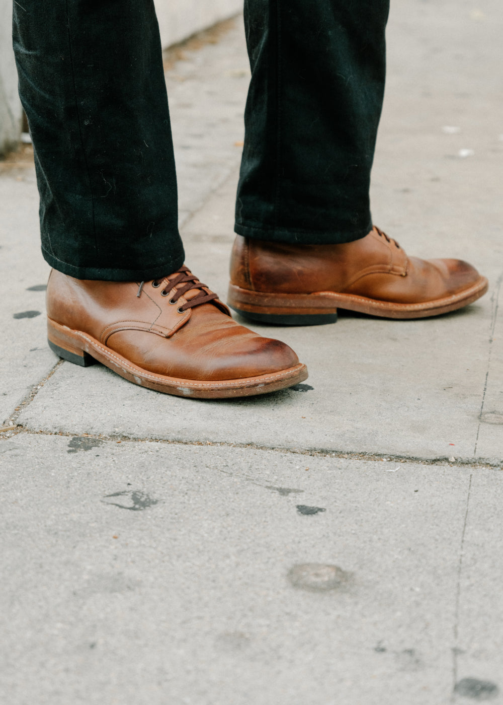 Brown leather shoes worn with black pants on a concrete surface