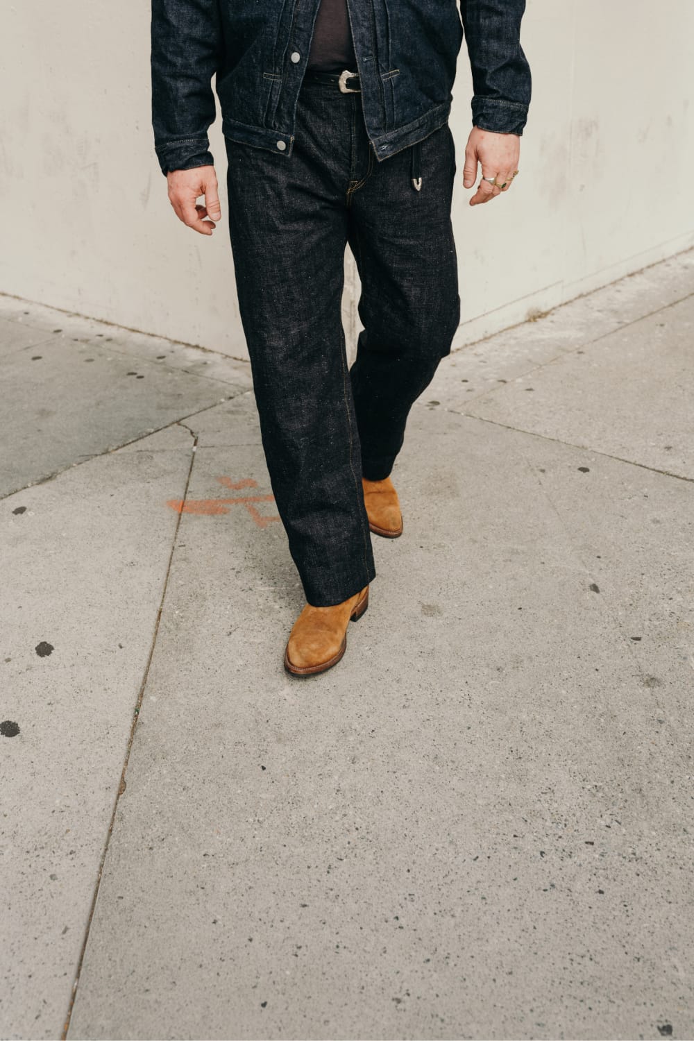 Person wearing dark jeans and brown boots on a sidewalk.