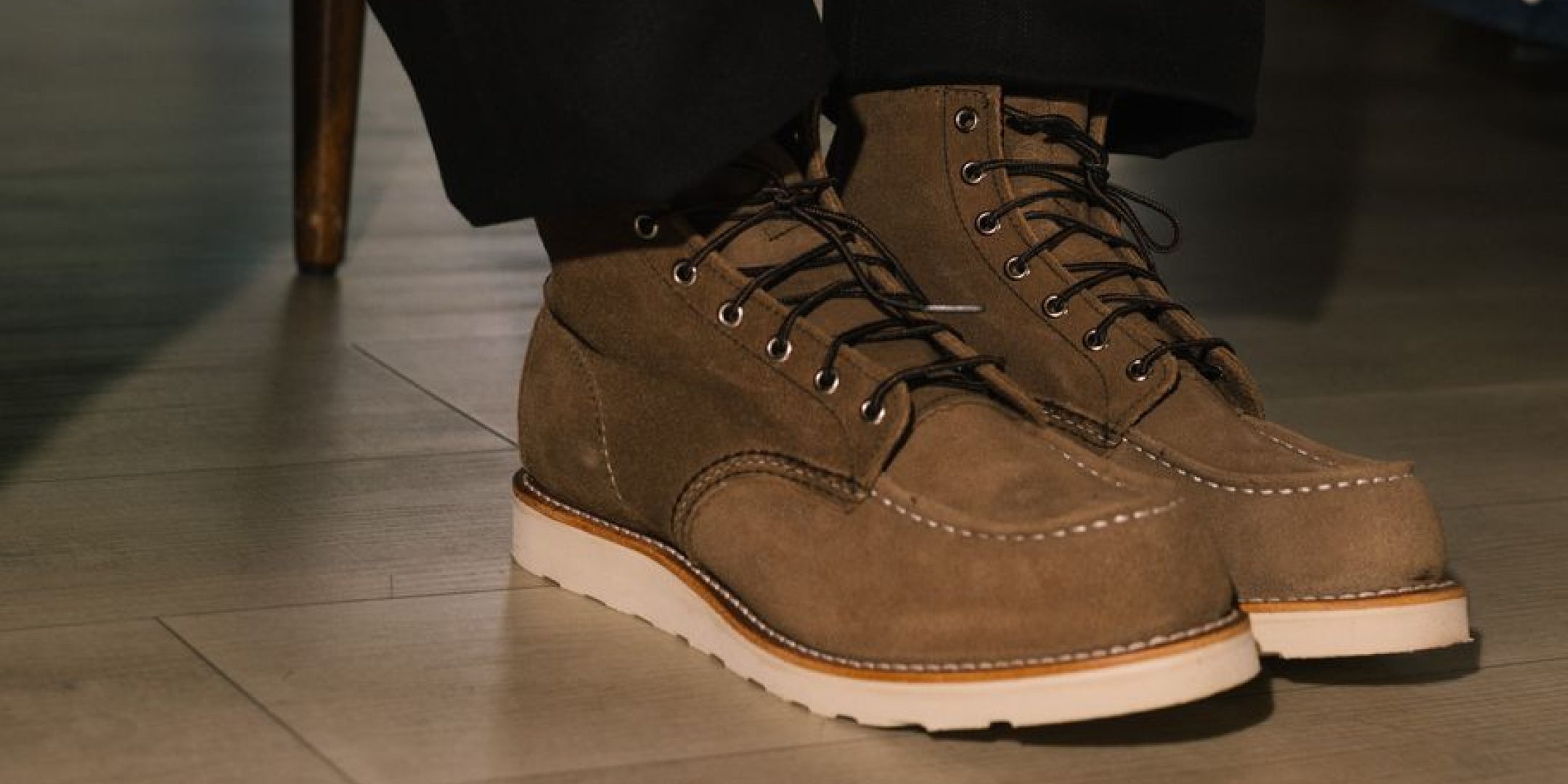 A person wearing brown suede lace-up work boots with black pants, sitting in a store or room setting.