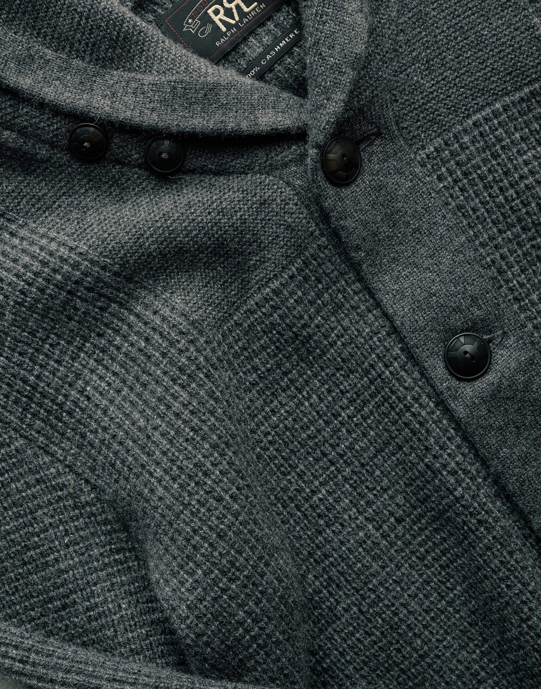 Close-up of a textured gray knitwear with buttons and a brand label.