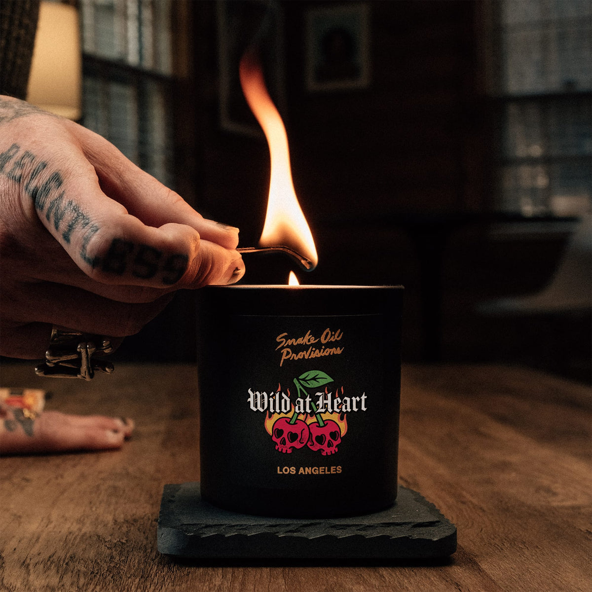 Hand lighting a candle with 'Wild at Heart' branding on a wooden surface.